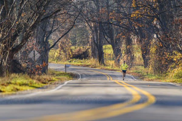 Mid-adult man running along scenic road in autumn