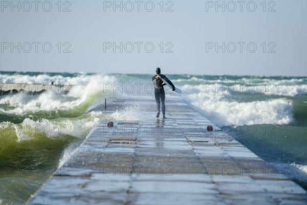 Rear view of surfer in wetsuit walking to end of pier