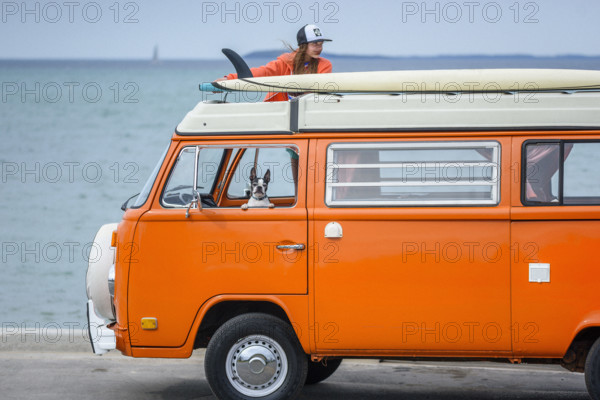 Young adult woman unloading paddle board from top of orange van