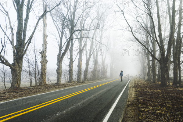 Rear view of mid-adult man skateboarding on foggy road