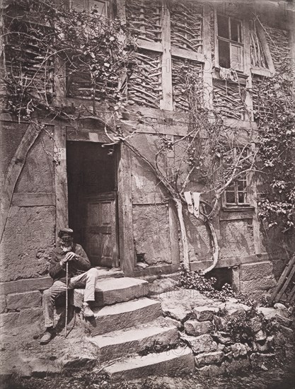 [Man Sitting on Steps of House with Socks Hanging on Nearby Vine to Dry], 1880s.