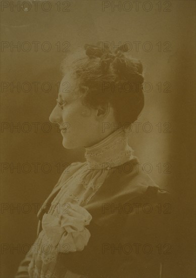 Studio portrait of young woman in white dress posed as if holding flowering tree branch, c1900.