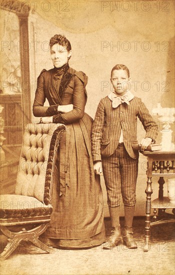 Unidentified standing figures: woman, her folded arms leaning on back of chair..., 1890. Creator: J. N. Wilson.