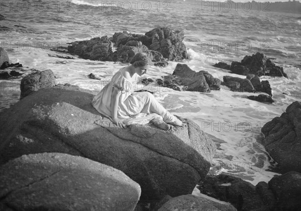 Wilson, Helen, Mrs., seated on rocks at the beach, between 1906 and 1928. Creator: Arnold Genthe.