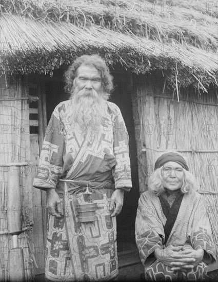 Ainu man and seated woman at the entrance of a hut, 1908. Creator: Arnold Genthe.