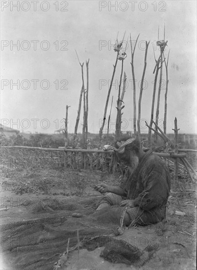 Ainu seated outside working on nets, 1908. Creator: Arnold Genthe.