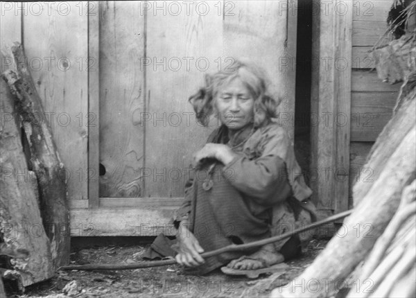 Ainu woman seated by the door of a wooden hut, 1908. Creator: Arnold Genthe.