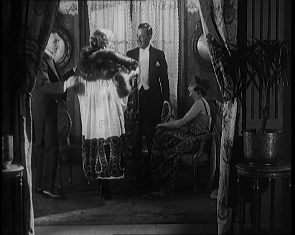 A Male Civilian Helping a Female Civilian Remove Her Fur Trimmed Coat Revealing an Ornated Gown, 192 Creator: British Pathe Ltd.