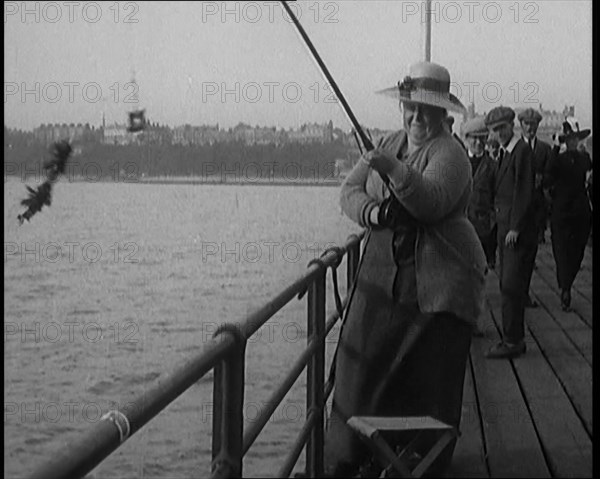 Female Civilian Wearing a Hat with a Dark Ribbon Fishing from a Pier, 1920. Creator: British Pathe Ltd.