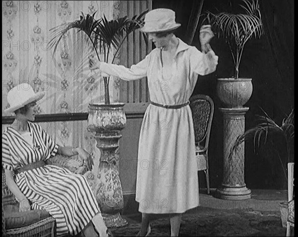 Two Female Civilians Leisuring in a Drawing Room Wearing Long Dresses and Hats Comparing..., 1920. Creator: British Pathe Ltd.