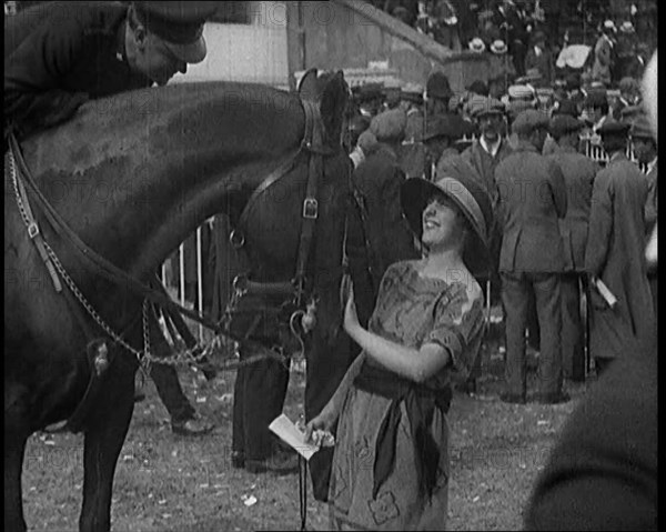 A Female Civilian Wearing a Dress and a Large Hat with a Ribbon Petting a Horse on the Nose at a Hor Creator: British Pathe Ltd.