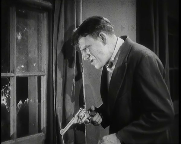 Scene from the Film 'The Informer':  Male Actor Shooting a Gun Out of a Window, 1920s. Creator: British Pathe Ltd.