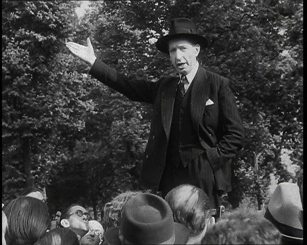 A Close up of a British Man in Dark Suit and Hat Declaiming Before a Crowd from a Raised..., 1938. Creator: British Pathe Ltd.