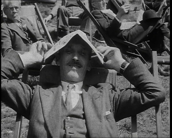 British Man in a Three Piece Suit Sitting in a Deckchair Smiling at the Camera and Holding..., 1938. Creator: British Pathe Ltd.