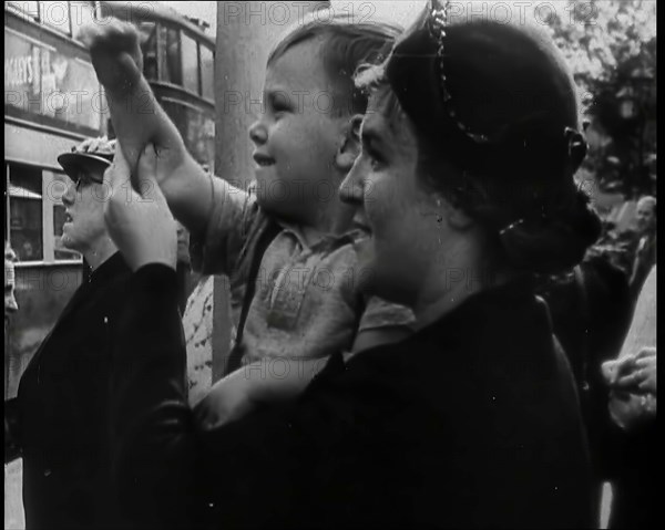 A British Woman Holding up a Young Boy Who is Waving in the Direction of a Bus as Other..., 1939. Creator: British Pathe Ltd.