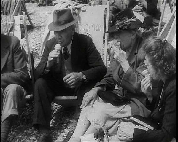 A Group of Two Men and Two Women Sitting on Deckchairs on the Beach at  Brighton and Eating..., 1939 Creator: British Pathe Ltd.