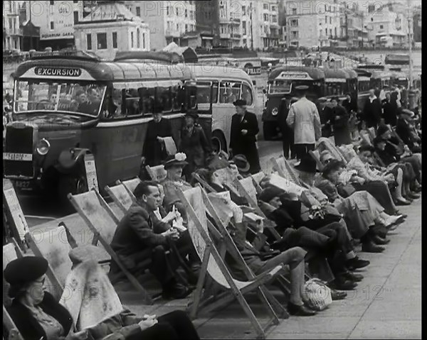 Men and Women Sitting in Deckchairs on the Promenade at  Brighton With a Row of Buses..., 1939. Creator: British Pathe Ltd.