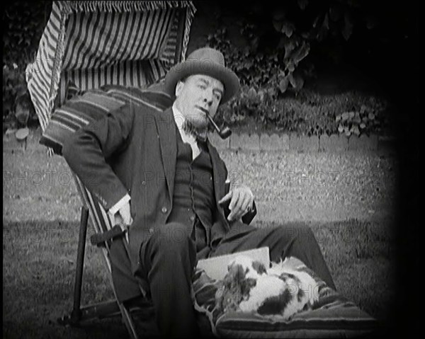 Matheson Lang Relaxing in a Deck Chair Smoking a Pipe With a Dog at His Feet, 1920s. Creator: British Pathe Ltd.