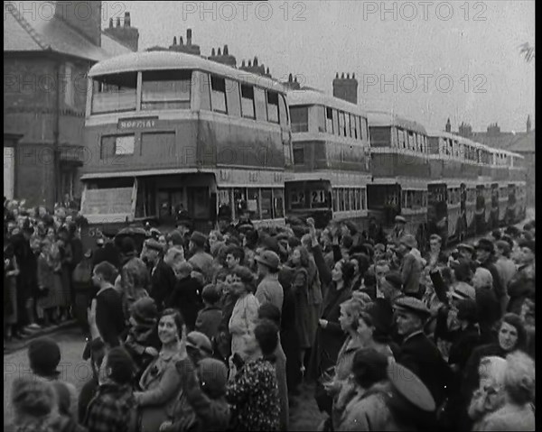 Men, Women, and Children Standing by a Line of Buses Parked in a Residential Street, 1939. Creator: British Pathe Ltd.