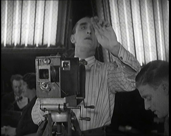 A Male Cameraman Films a Scene Whilst Lights Illuminate Behind Him, 1920s. Creator: British Pathe Ltd.