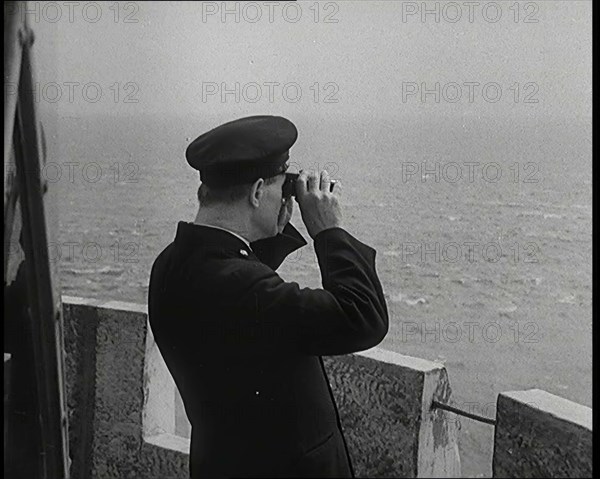 Lighthouse Keeper Looking Through Binoculars at the Turbulent Sea, 1920s. Creator: British Pathe Ltd.