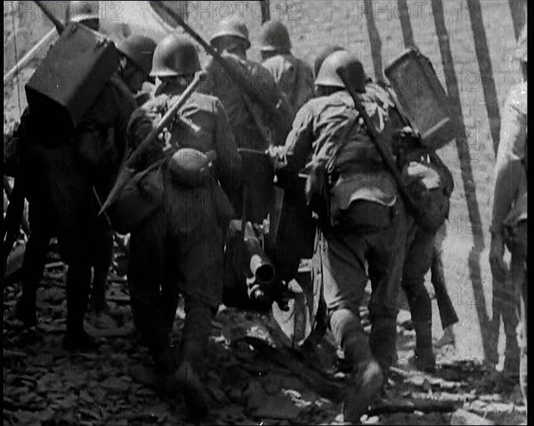 A Group of Male Japanese Soldiers Pushing a Gun Over Rubble in a Street in Shanghai, 1937. Creator: British Pathe Ltd.