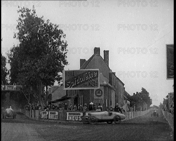 A Racing Circuit As Racing Cars Drive By. Signs On a Building Read: 'Spidoleine Huile' and..., 1924. Creator: British Pathe Ltd.