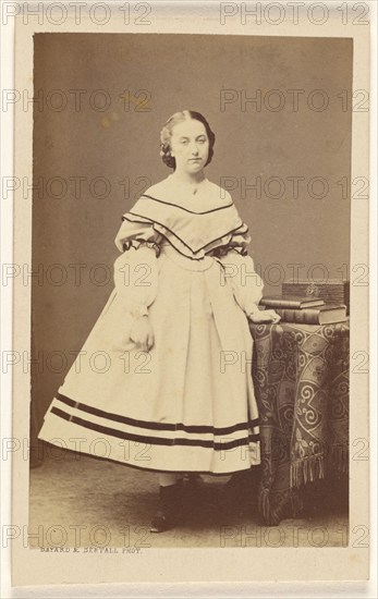 Unidentified woman standing near a table with books on top, 1865-1875. Creator: Bayard & Bertall.