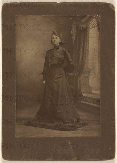 Portrait of a young woman in long black dress, standing, about 1900. Creator: George W Killian.