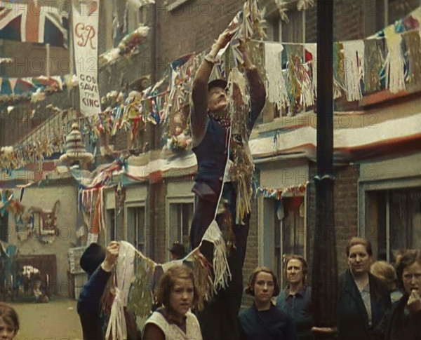 Man Hanging Bunting from a Lamp Post in a Street With Decorations For the Coronation of..., 1937. Creator: British Pathe Ltd.