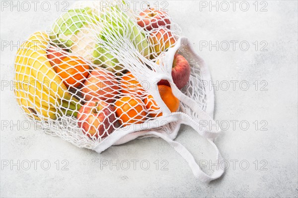 Zero waste eco friendly shopping concept, vegetables fruits in white mesh bag on white kitchen table, selective focus