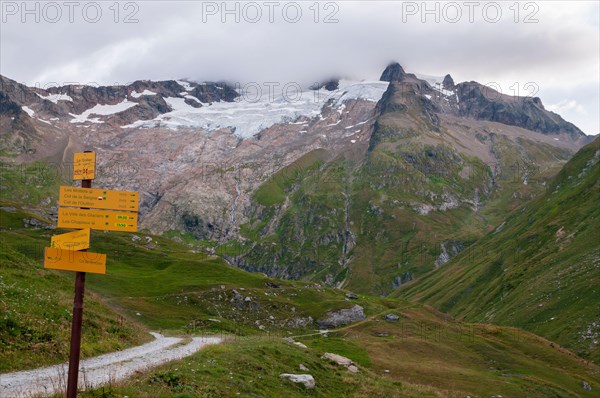 Hiking signposts on the GR Tour du Mont-Blanc trail near the refuge des Mottets with view of the glacier des Glaciers, Chapieux Valley, Savoie (73), A