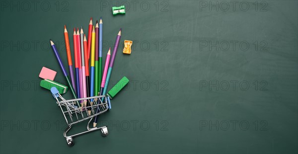 Miniature shopping cart full of school office supplies on a green chalk board. Preparing for school, buying pens and notebooks