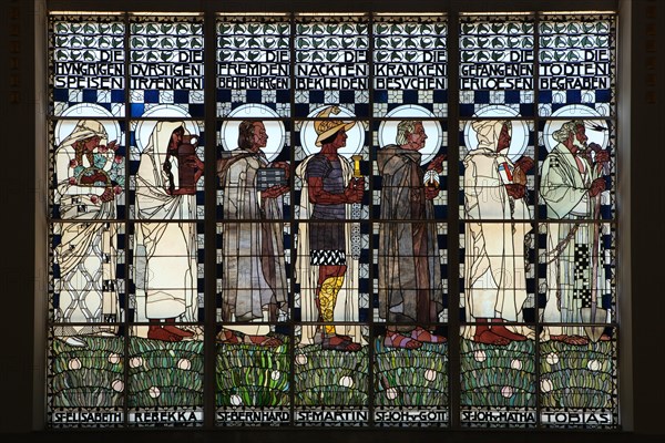 Stained glass window 'The Seven Corporal Works of Mercy' designed by Austrian artist Koloman Moser (1907) in the Steinhof Church (Kirche am Steinhof) in Vienna, Austria. Saints and Old Testaments characters are depicted in the stained glass window from left to right: Saint Elizabeth of Hungary, Rebecca, Saint Bernard, Saint Martin of Tours, Saint John of God, Saint John of Matha and Tobias.