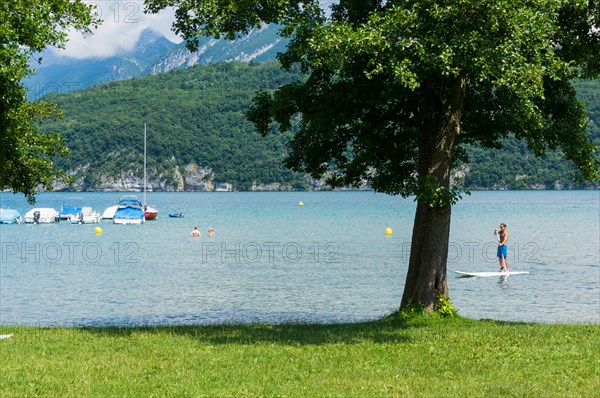 Man on a paddleboard on Lake Annecy, Haute-Savoie, France, Europe with swimmers in summer