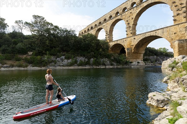 Mother and son stand up paddling (SUP) on the Gardon river and Pont du Gard, Provence, France.