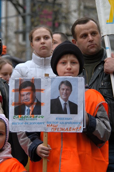 Orange revolution in Ukraine. Young boy dressed orange attends the demonstration of Ukrainian migrants in the Czech Republic to support Ukrainian oppositional presidential candidate Viktor Yushchenko in Wenceslas Square in Prague, Czech Republic, on November 28, 2004. The inscription under the portrait of presidential candidate Viktor Yanukovych (L) is changed to Bandukovych (literally a bandit or a robber). The inscription under the portrait of presidential candidate Viktor Yushchenko (R) is added with words 'Our President'.