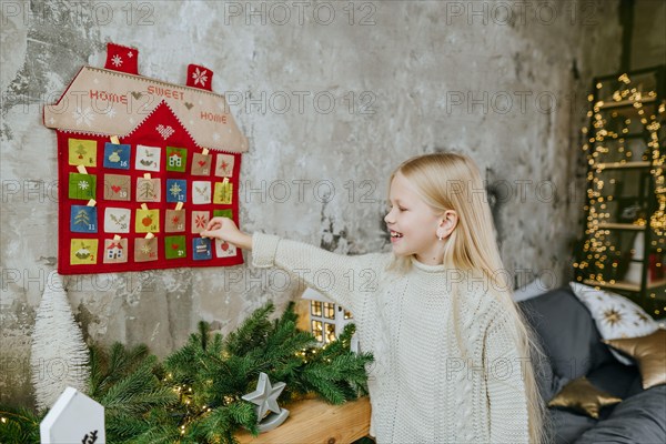 Girl getting a task out from the Christmas handmade advent calendar in a house shape to countdown the days until Christmas.