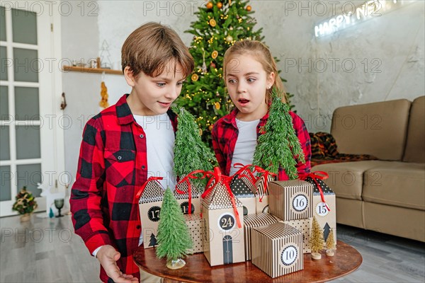 Children opening Christmas handmade advent calendar in a house shape to countdown the days until Christmas in the room.