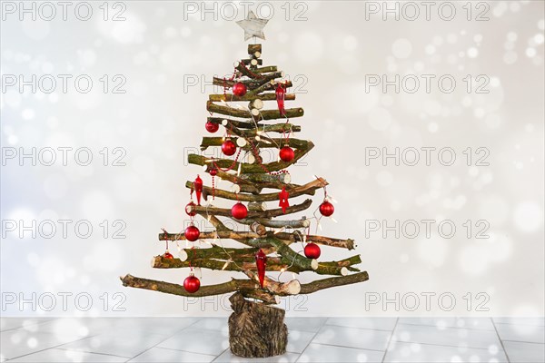 Alternative homemade Christmas tree made of rustic raw wood branches, with fairy lights and red baubles, sustainable craft for eco friendly holidays,