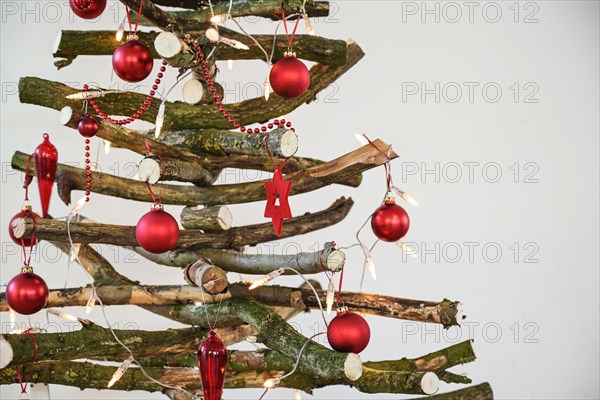 Homemade rustic Christmas tree made of raw wood branches, decorated with fairy lights and red balls, sustainable and environmentally friendly alternat