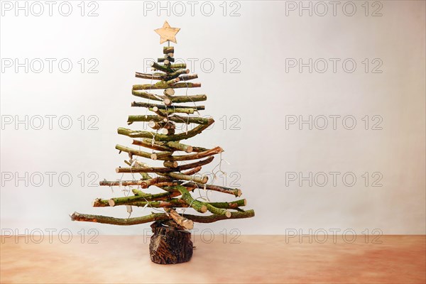 Rustic Christmas tree made of raw wood branches decorated with fairy lights and a star, homemade sustainable and eco friendly alternative for the holi