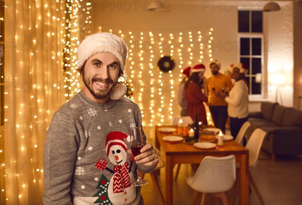 Portrait of happy man in ugly Christmas sweater and Santa hat at Christmas party