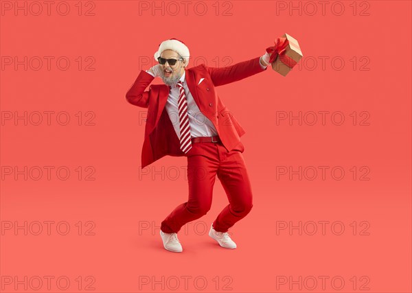 Cool energetic man in santa hat having fun and dancing with christmas gift in hand.