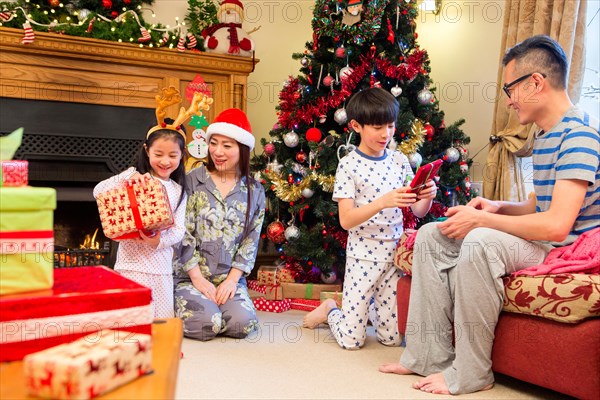 Chinese family opening presents together on Christmas morning. They are all sitting in the front room in their pyjamas