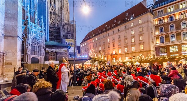 Vienna, Austria, 06th December 2017. St Nicholas (Nikolaus) appears before a crowd of children helpers in traditional red and white Santa hats in the winter festive season Christmas market in Stephansplatz by Stephansdom cathedral.  The children are given chocolates and sweets after Nikolaus' appearance.  Credit: Graham Prentice/Alamy Live News