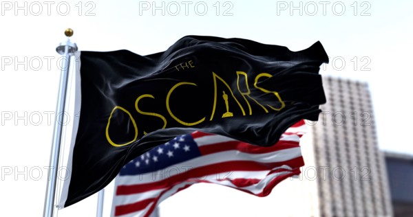 Hollywood, CA, USA, March 2022: the flag with the Academy Awards logo waving with the American flag blurred in the background. The Academy Award, aka