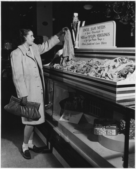 Part of a campaign to collect used nylon stockings for American efforts during World War II, a young woman holds up a pair of disbanded stockings that will be recycled into gun powder bags, 1942. Image courtesy National Archives.