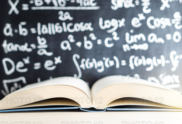 Knowledge, education, mathematics, science and wisdom concept. Open book in front of a blackboard and chalkboard full of math writing.