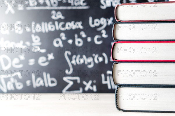 Stack and pile of books in front of a blackboard in school. Math equation handwritten on chalkboard.